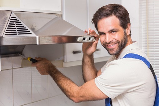 Smiling technician repairing a range hood fan in a Winnipeg kitchen