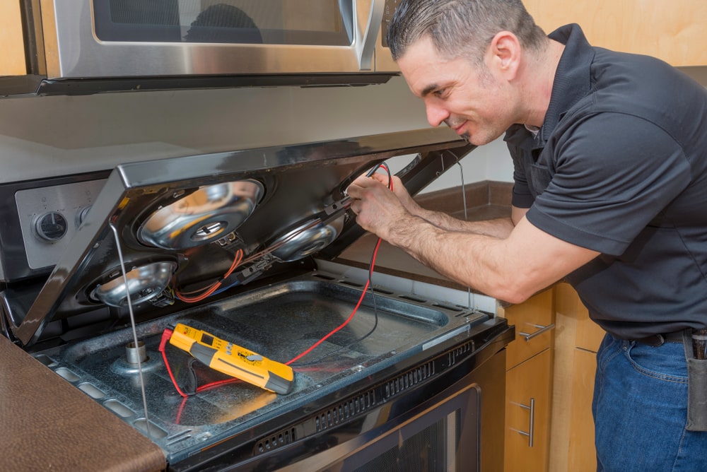 Appliance technician testing a gas stove and cooktop with a multimeter in Winnipeg